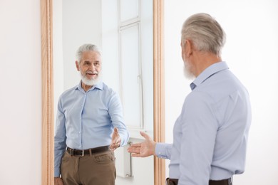Photo of Handsome senior man looking at himself in mirror indoors