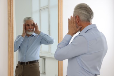 Photo of Handsome senior man looking at himself in mirror indoors