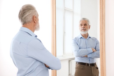 Photo of Handsome senior man looking at himself in mirror indoors