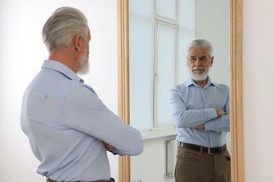 Photo of Handsome senior man looking at himself in mirror indoors