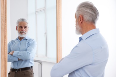 Photo of Handsome senior man looking at himself in mirror indoors