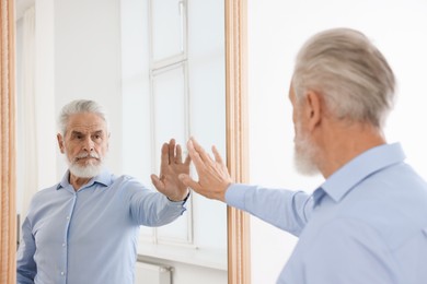 Photo of Handsome senior man looking at himself in mirror indoors