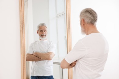 Photo of Handsome senior man looking at himself in mirror indoors