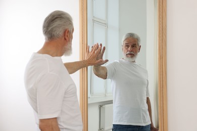 Photo of Handsome senior man looking at himself in mirror indoors