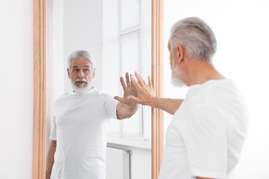 Photo of Handsome senior man looking at himself in mirror indoors