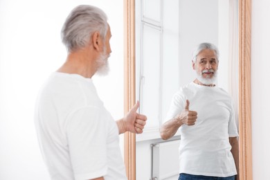 Photo of Handsome senior man showing thumbs up mirror indoors