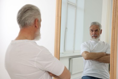 Photo of Handsome senior man looking at himself in mirror indoors
