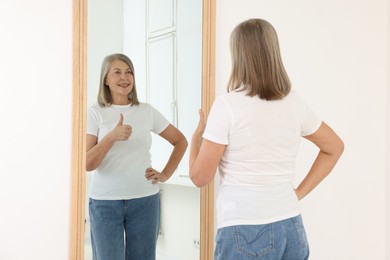 Photo of Beautiful senior woman showing thumbs up near mirror indoors
