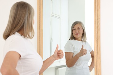Photo of Beautiful senior woman showing thumbs up near mirror indoors