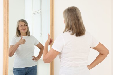 Photo of Beautiful senior woman showing thumbs up near mirror indoors