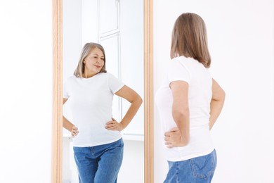 Photo of Beautiful senior woman looking at herself in mirror indoors
