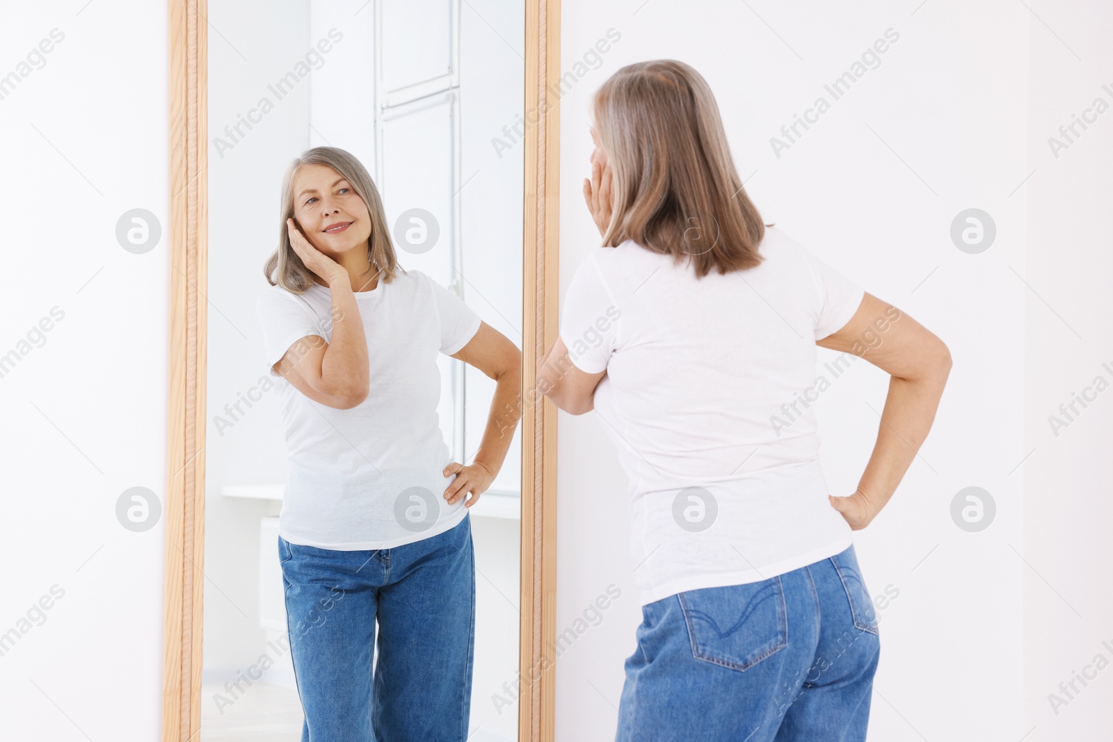 Beautiful senior woman looking at herself in mirror indoors Photo of Beautiful senior woman looking at herself in mirror indoors
