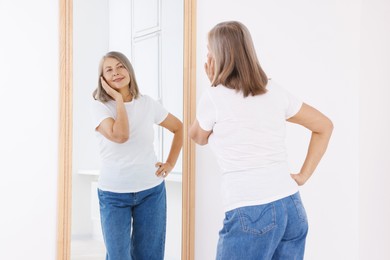 Photo of Beautiful senior woman looking at herself in mirror indoors
