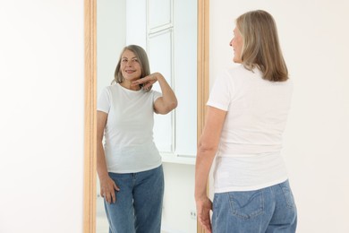 Photo of Beautiful senior woman looking at herself in mirror indoors