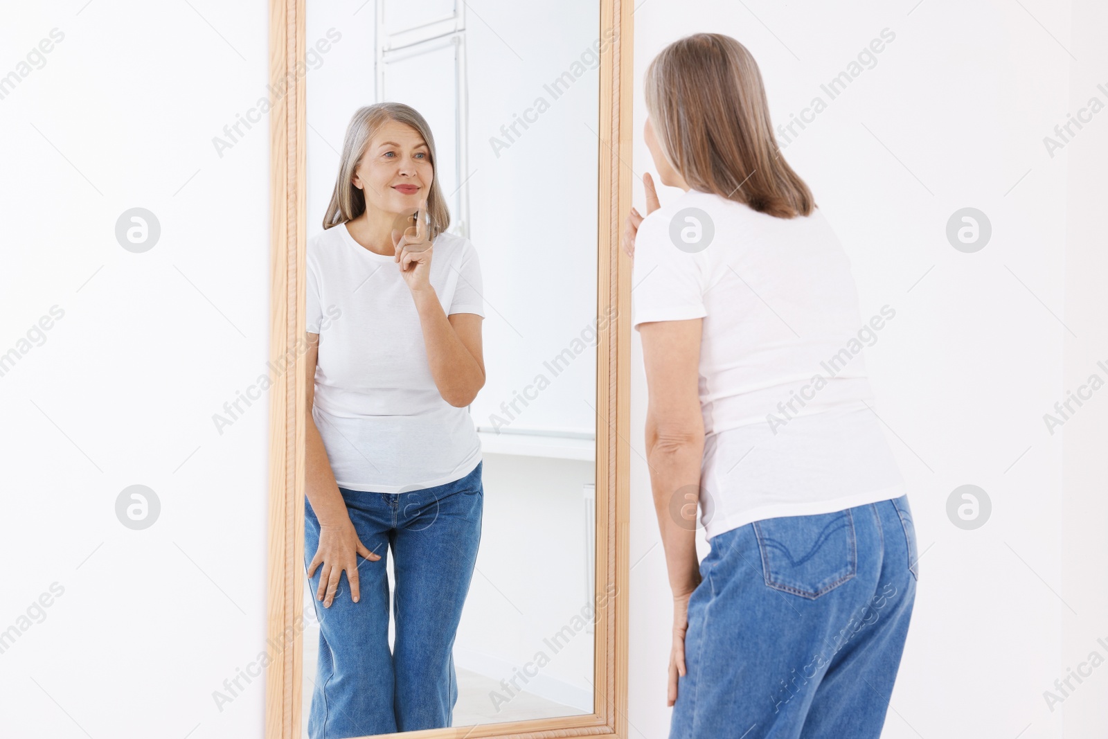 Beautiful senior woman looking at herself in mirror indoors Photo of Beautiful senior woman looking at herself in mirror indoors
