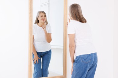 Photo of Beautiful senior woman looking at herself in mirror indoors