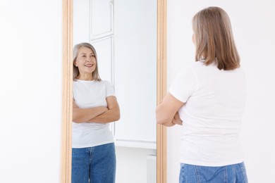 Photo of Beautiful senior woman looking at herself in mirror indoors