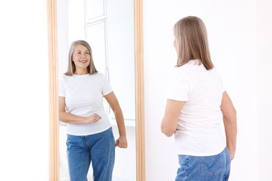 Photo of Beautiful senior woman looking at herself in mirror indoors