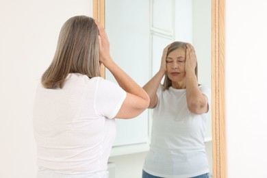 Photo of Beautiful senior woman near mirror indoors, selective focus