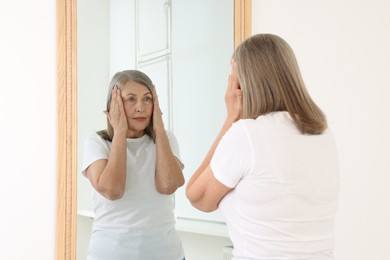 Photo of Beautiful senior woman looking at herself in mirror indoors