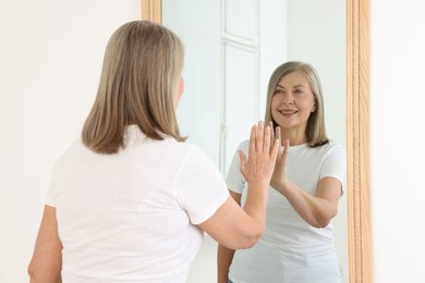 Photo of Beautiful senior woman looking at herself in mirror indoors