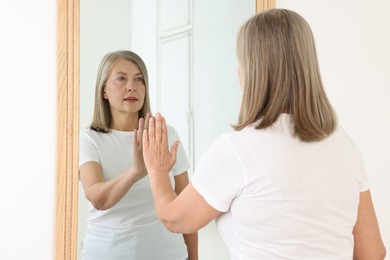 Photo of Beautiful senior woman looking at herself in mirror indoors