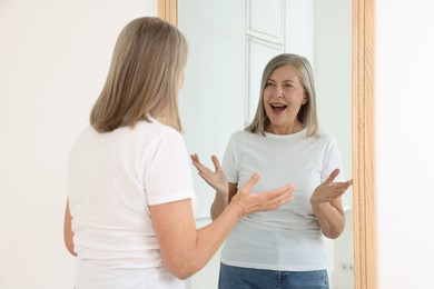 Photo of Beautiful senior woman looking at herself in mirror indoors