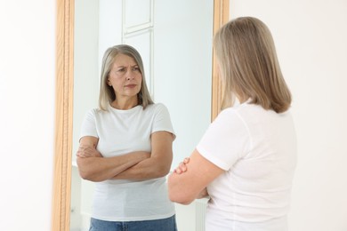 Photo of Beautiful senior woman looking at herself in mirror indoors