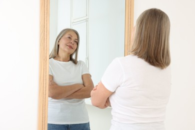 Photo of Beautiful senior woman looking at herself in mirror indoors