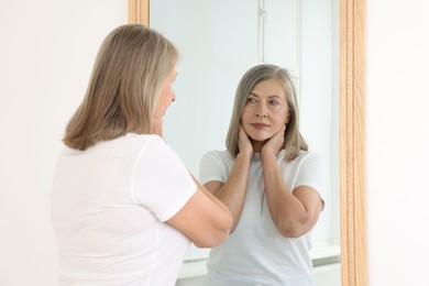 Photo of Beautiful senior woman looking at herself in mirror indoors