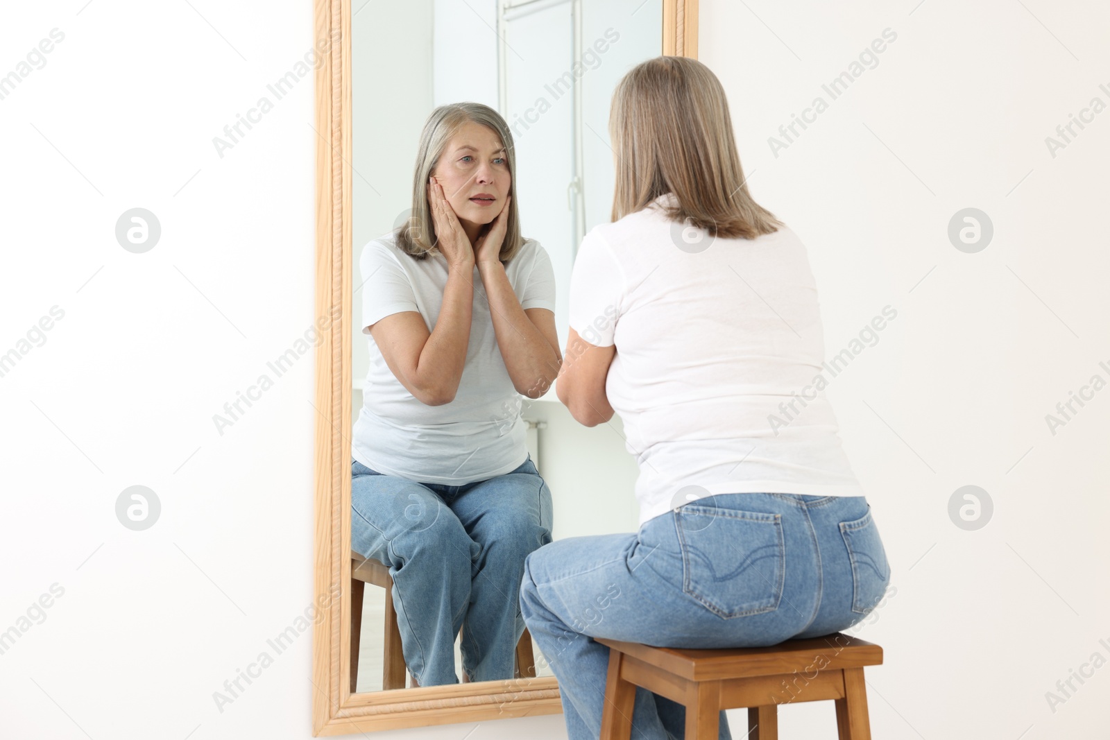 Beautiful senior woman looking at herself in mirror indoors Photo of Beautiful senior woman looking at herself in mirror indoors