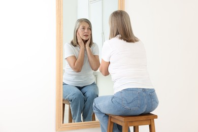 Photo of Beautiful senior woman looking at herself in mirror indoors