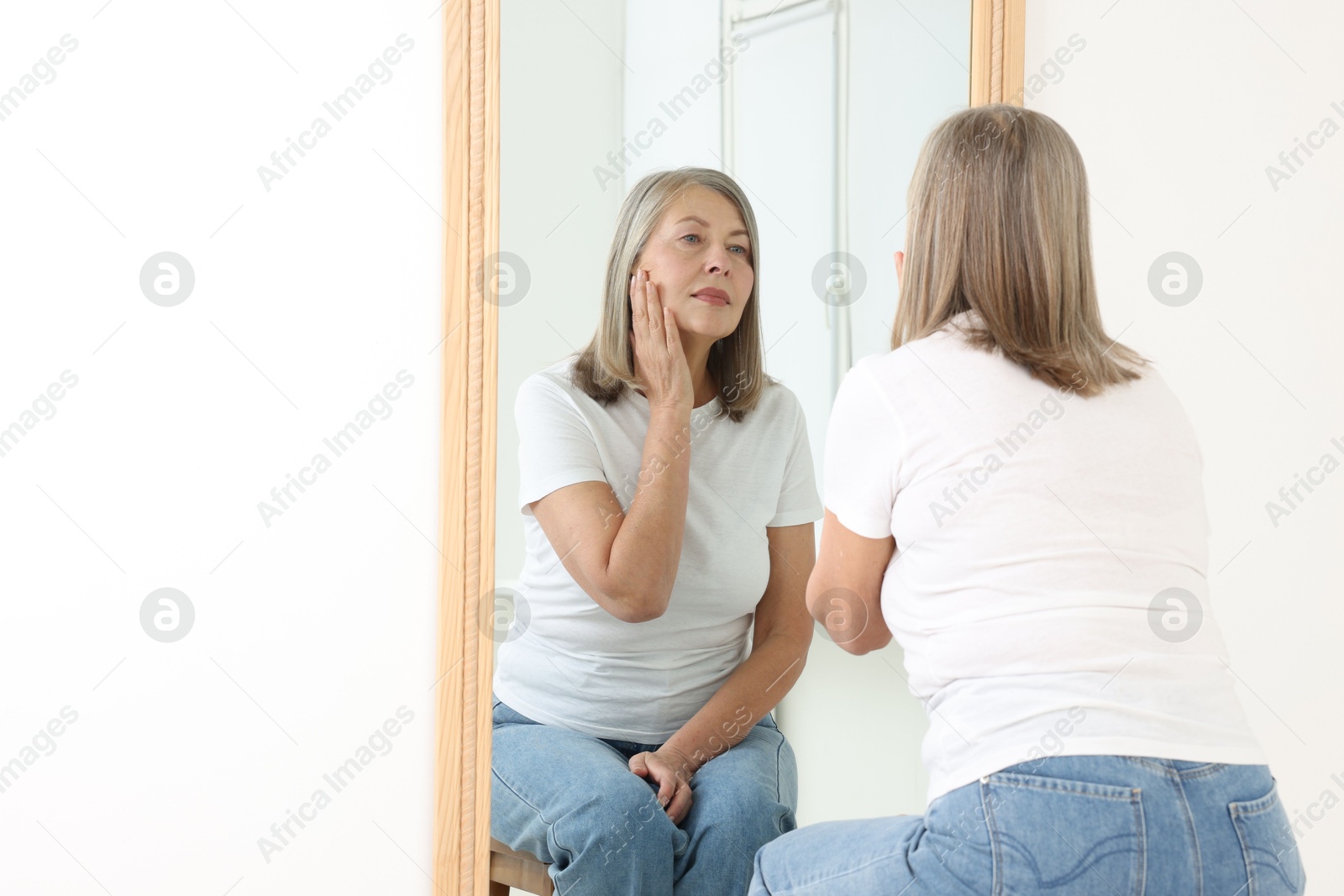 Beautiful senior woman looking at herself in mirror indoors Photo of Beautiful senior woman looking at herself in mirror indoors