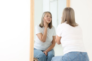 Photo of Beautiful senior woman looking at herself in mirror indoors