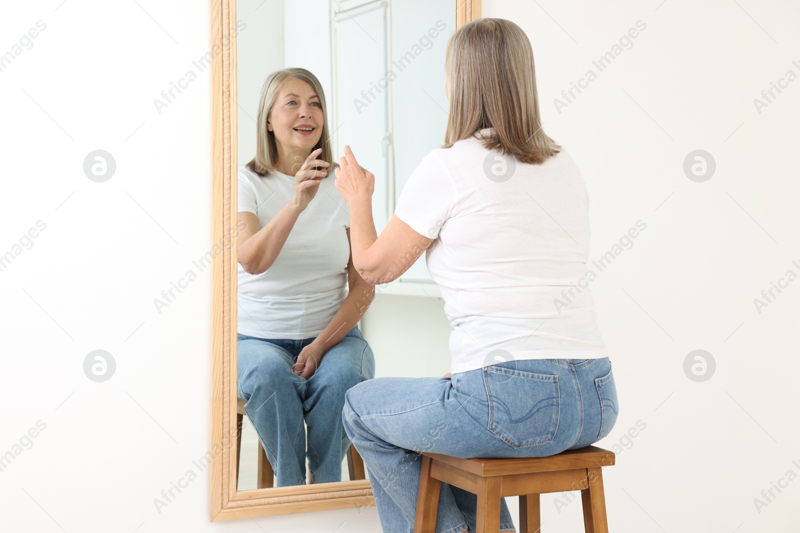 Beautiful senior woman looking at herself in mirror indoors Photo of Beautiful senior woman looking at herself in mirror indoors