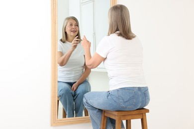 Photo of Beautiful senior woman looking at herself in mirror indoors