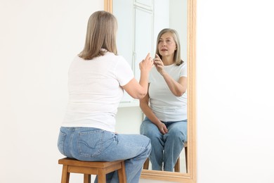 Photo of Beautiful senior woman looking at herself in mirror indoors