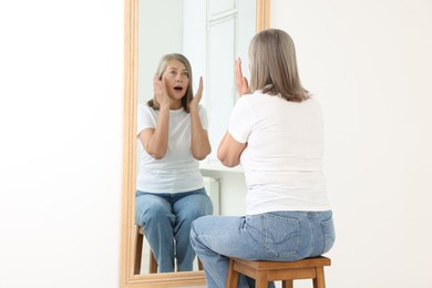 Photo of Beautiful senior woman looking at herself in mirror indoors