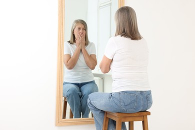 Photo of Beautiful senior woman looking at herself in mirror indoors
