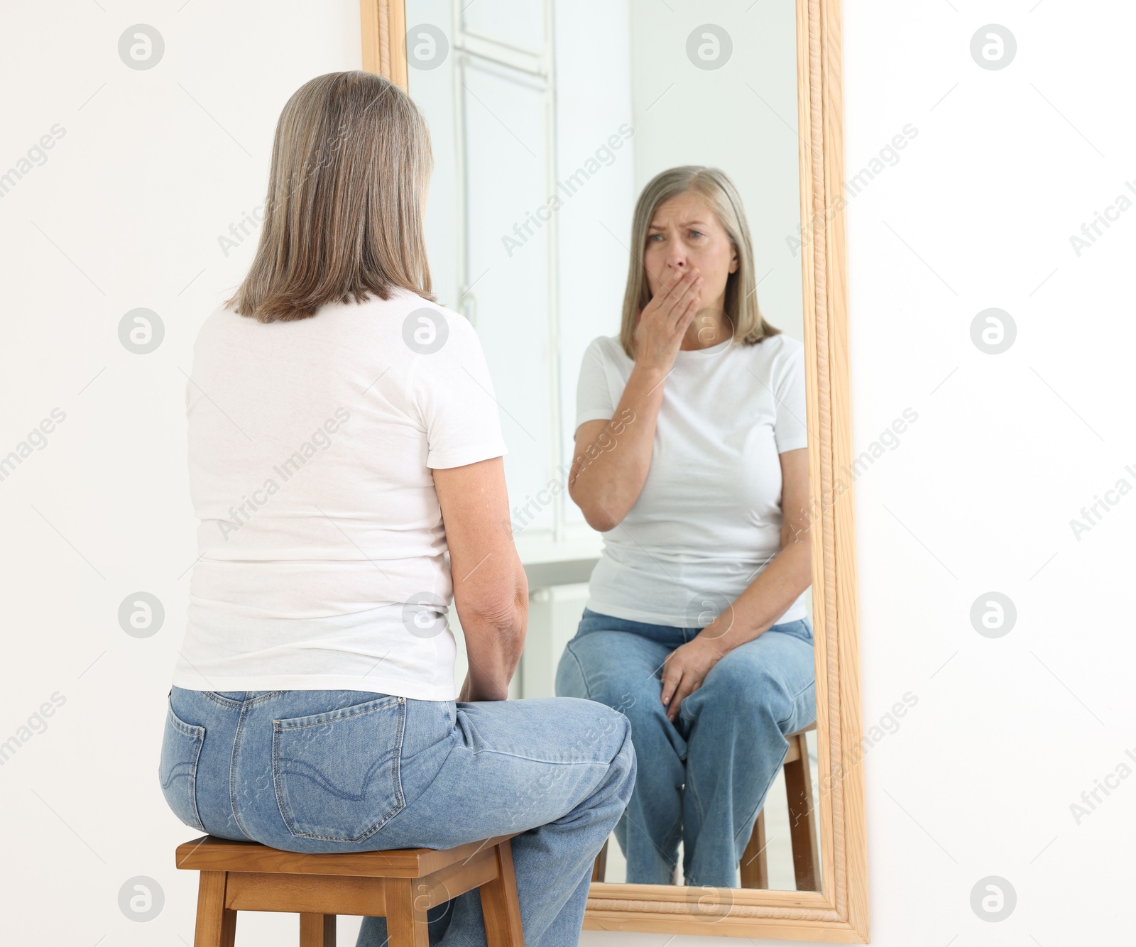 Beautiful senior woman looking at herself in mirror indoors Photo of Beautiful senior woman looking at herself in mirror indoors