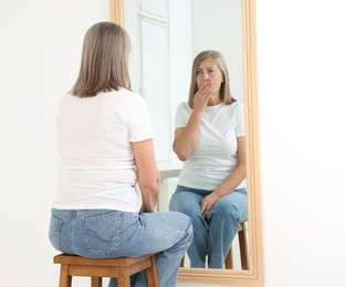 Photo of Beautiful senior woman looking at herself in mirror indoors