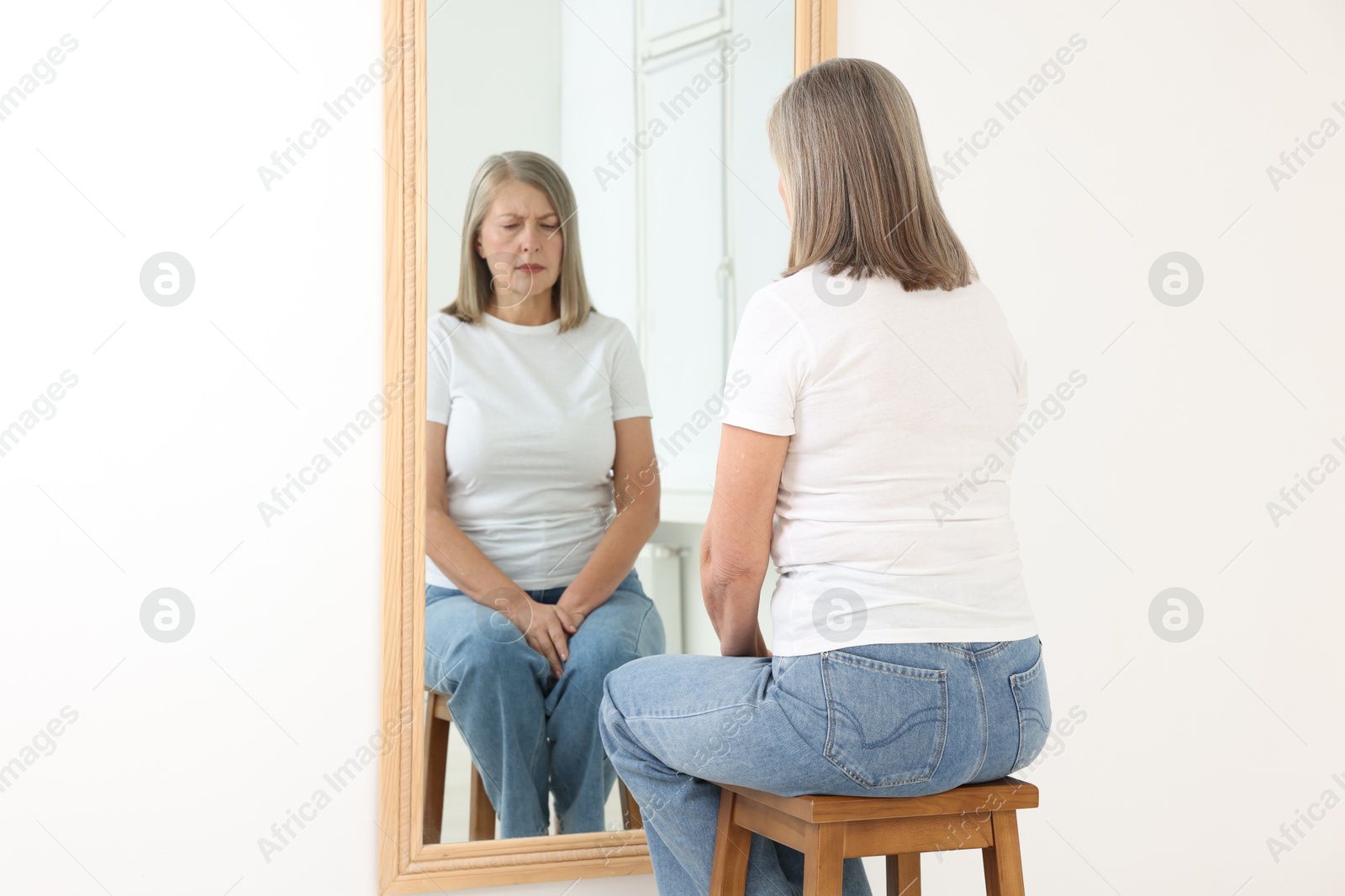 Beautiful senior woman looking at herself in mirror indoors Photo of Beautiful senior woman looking at herself in mirror indoors