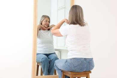 Photo of Beautiful senior woman looking at herself in mirror indoors