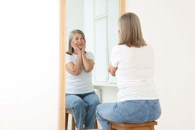 Photo of Beautiful senior woman looking at herself in mirror indoors