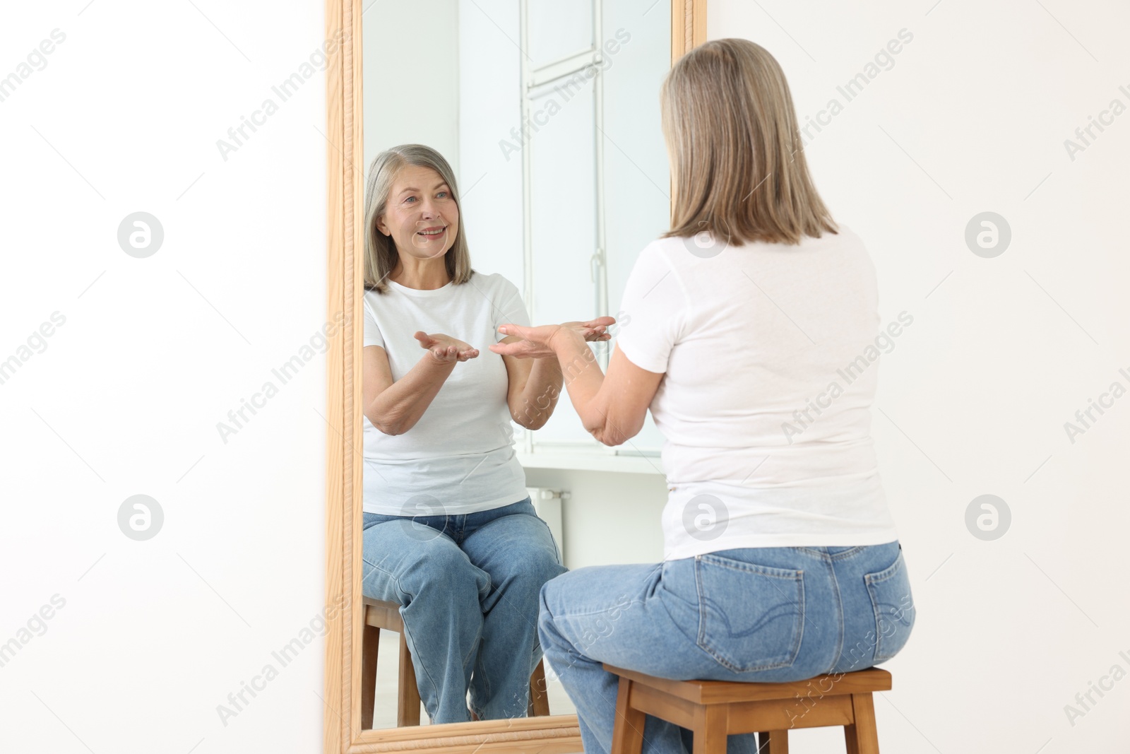 Beautiful senior woman looking at herself in mirror indoors Photo of Beautiful senior woman looking at herself in mirror indoors