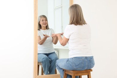 Photo of Beautiful senior woman looking at herself in mirror indoors