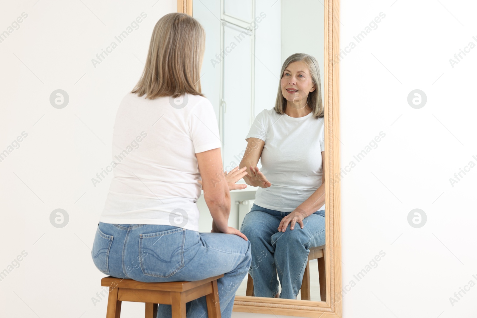Beautiful senior woman looking at herself in mirror indoors Photo of Beautiful senior woman looking at herself in mirror indoors