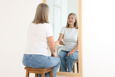 Photo of Beautiful senior woman looking at herself in mirror indoors