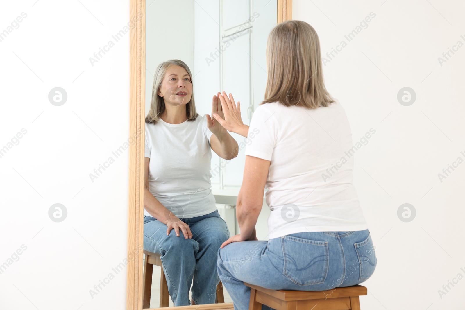 Beautiful senior woman looking at herself in mirror indoors Photo of Beautiful senior woman looking at herself in mirror indoors