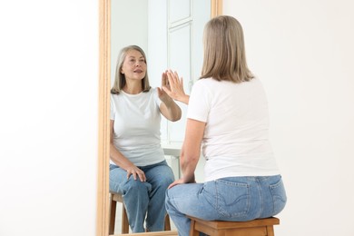 Photo of Beautiful senior woman looking at herself in mirror indoors